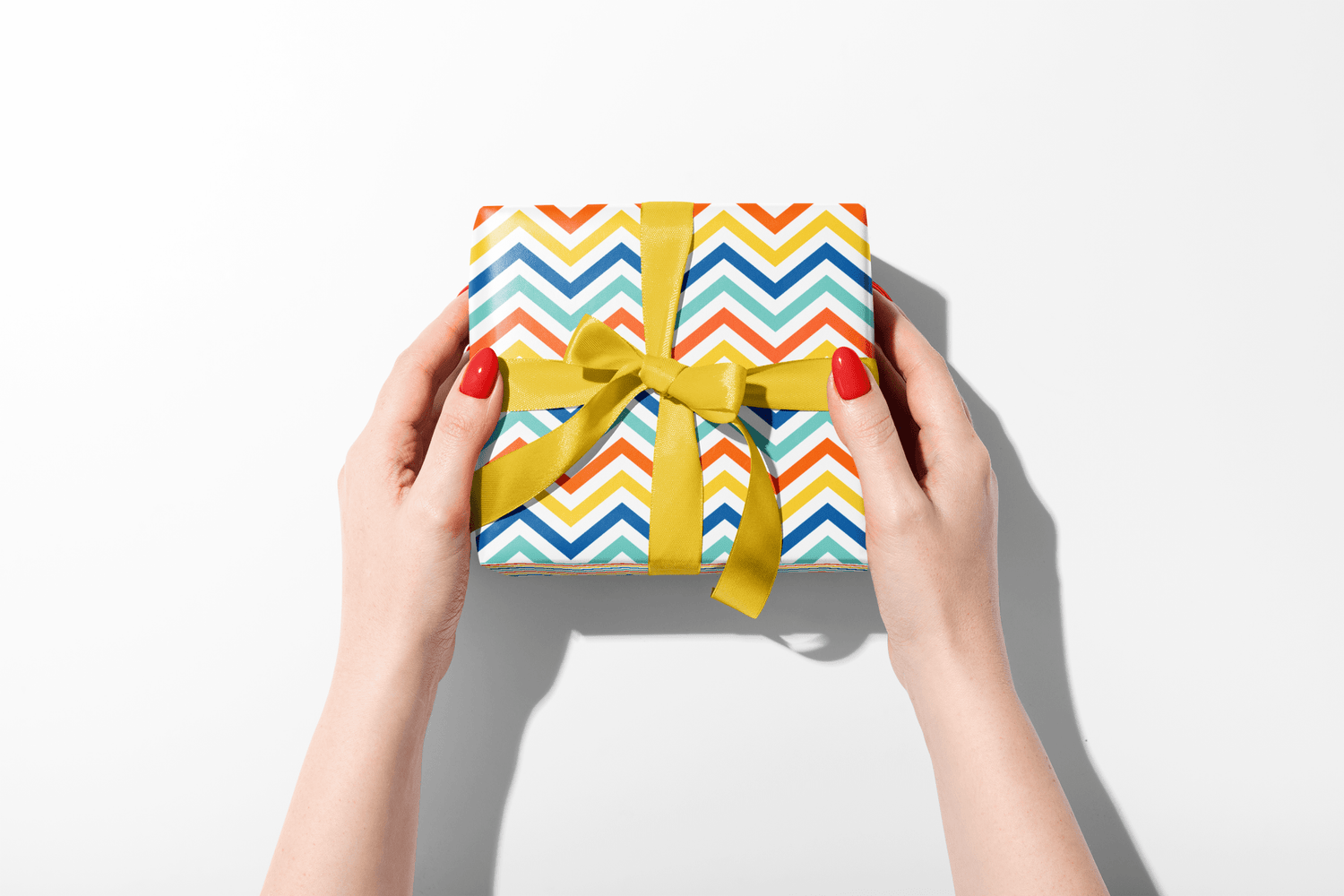 Colorful gift box with a yellow ribbon held by hands on a white background