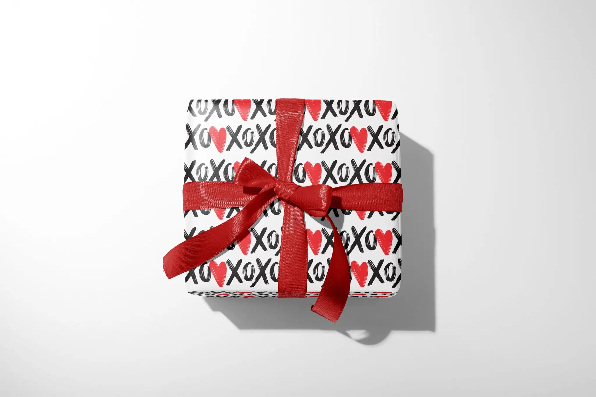 Playful XOXO Valentine Wrapping Paper on gift box with red ribbon bow, black and red XO heart pattern, Valentine’s present wrap