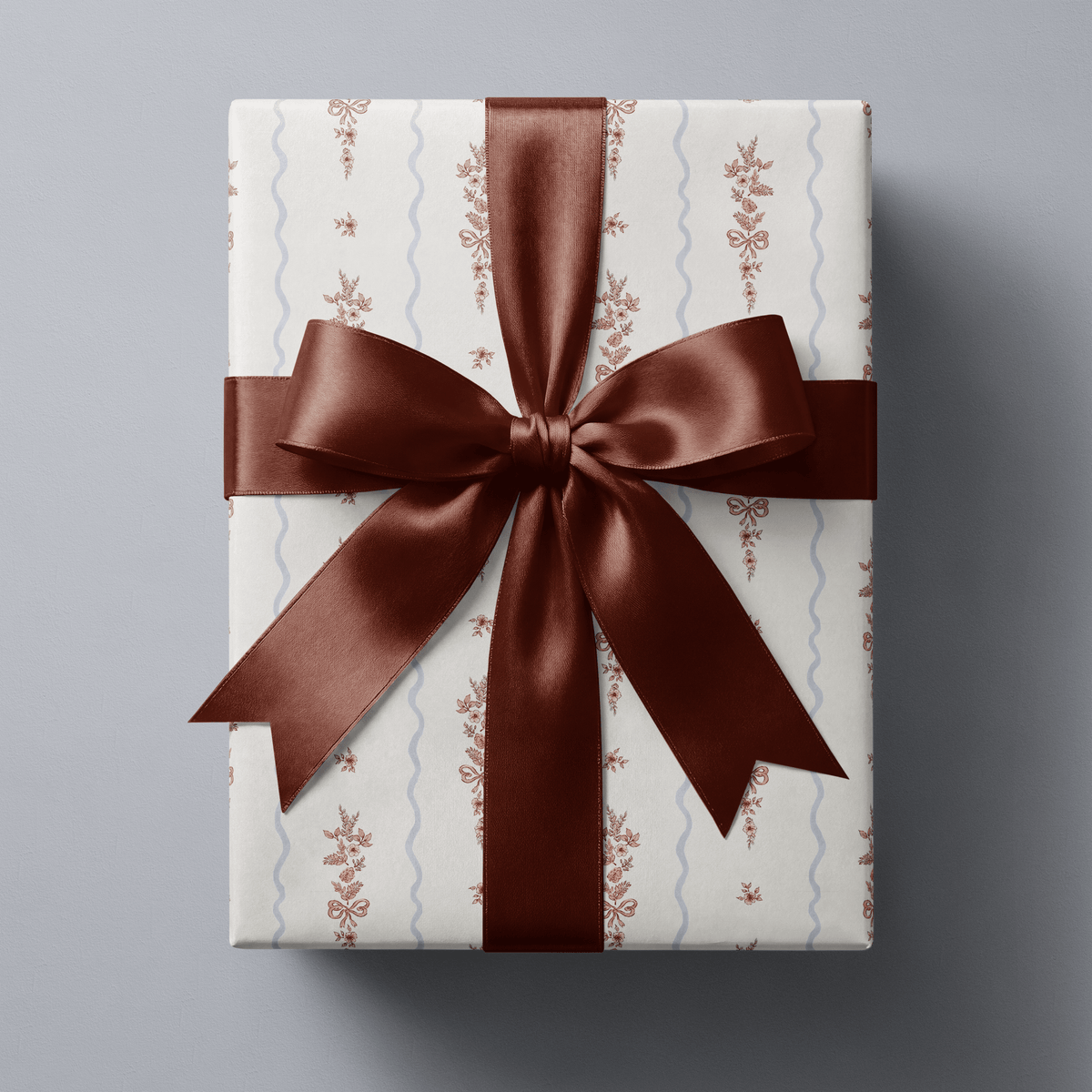 Floral Christmas wrapping paper with rose-pink botanical sprigs and little bows on white, divided by pale blue scallop stripes.
