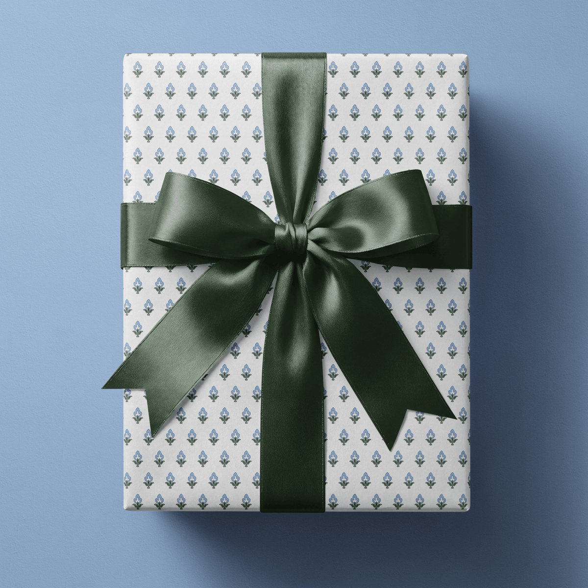 Blue floral wrapping paper with small blue and green block-print buds in a fine even repeat on white, finished with a navy satin bow.