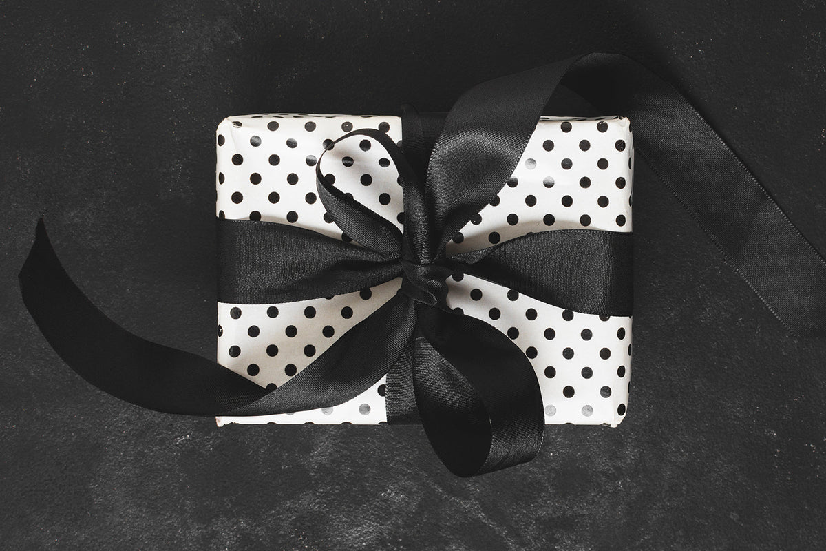 luxury gift presentation guide black and white polka dot wrapped gift with wide satin ribbon on dark background
