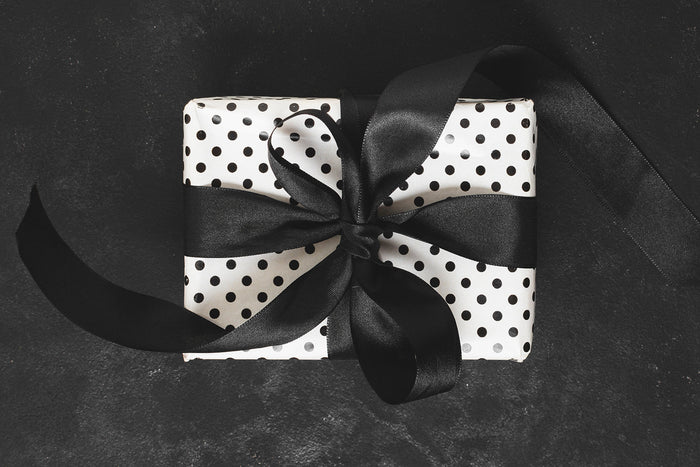 luxury gift presentation guide black and white polka dot wrapped gift with wide satin ribbon on dark background