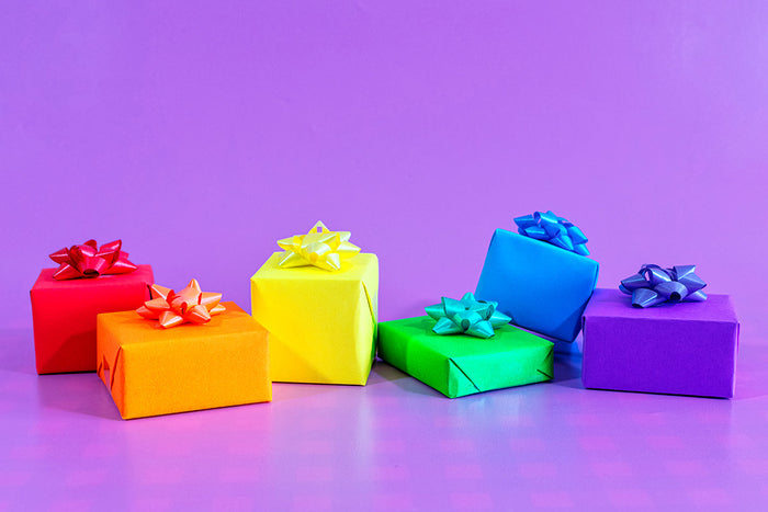Vibrant rainbow gift boxes with colorful bows on purple background, bold color psychology in luxury gift wrapping and expressive gift presentation.