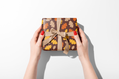Dense fall wrapping paper with a scattered pattern of stylized leaves in burnt orange, brown, and yellow, ideal for autumn and Thanksgiving gifts.
