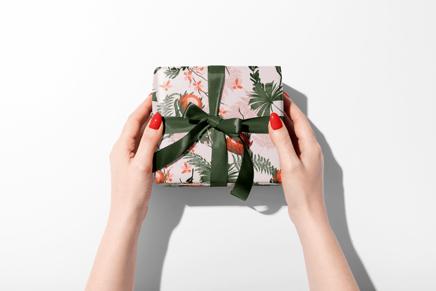 Gift box with floral pattern and green ribbon held by hands on a white background