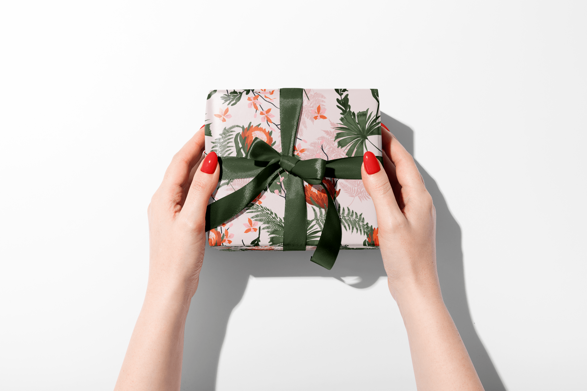 Gift box with floral pattern and green ribbon held by hands on a white background