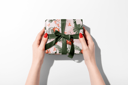 Gift box with floral pattern and green ribbon held by hands on a white background
