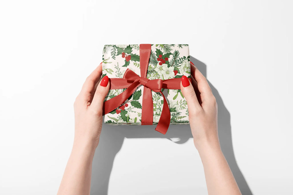 Botanical Christmas Wrapping Paper Petal Botanica gift wrap with holly berries, green foliage, white roses and red ribbon