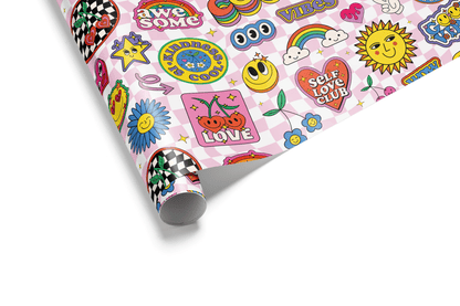 Pink and white checkerboard wrapping paper with a dense collage of colorful retro stickers, including emoji faces, rainbows, cherries, and positive slogans.