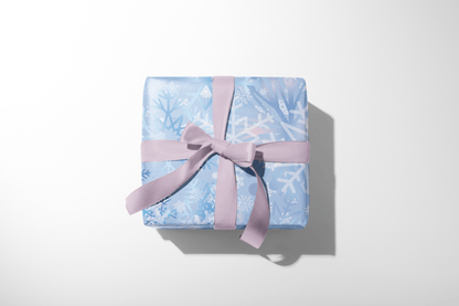 Christmas wrapping paper with an artistic, multi-layered pattern of watercolor snowflakes in shades of blue, lavender, and white, ideal for winter wonderland themes.
