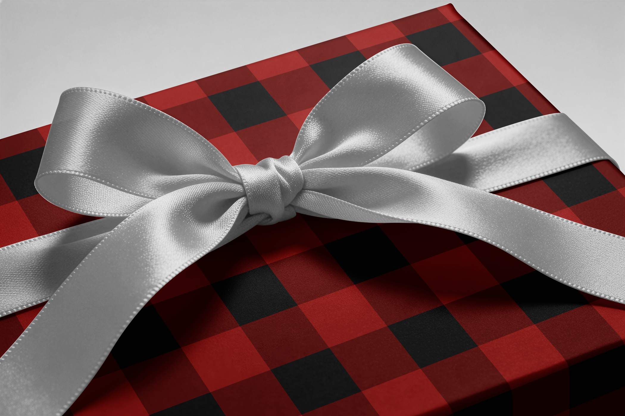 Buffalo Plaid Wrapping Paper in red and black tartan grid with silver satin ribbon bow on gift box, winter lodge style