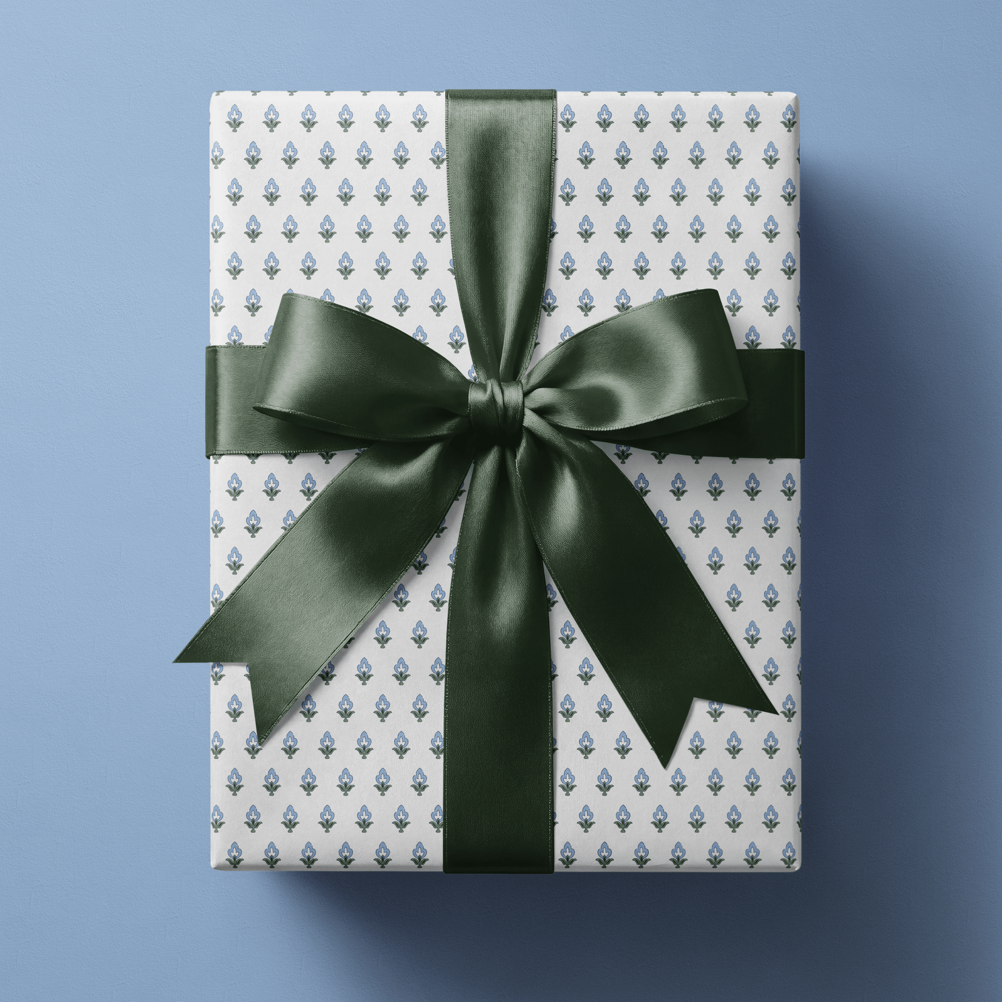 Blue floral wrapping paper with small blue and green block-print buds in a fine even repeat on white, finished with a navy satin bow.