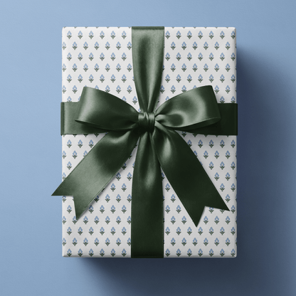 Blue floral wrapping paper with small blue and green block-print buds in a fine even repeat on white, finished with a navy satin bow.