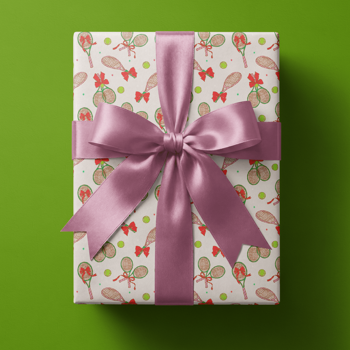 Tennis wrapping paper with hand-drawn rackets, tennis balls and little red bows in pink, green and red on cream, finished with a coral satin bow.