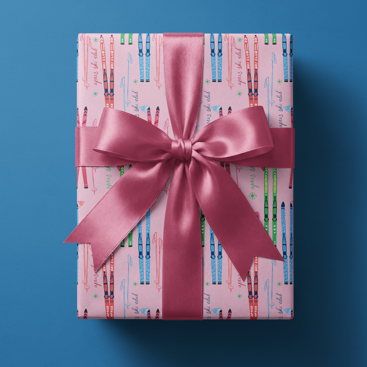 Skier wrapping paper with crossed skis, mittens, and snowflakes on bright pink, finished with a cream satin bow.