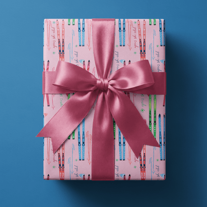 Skier wrapping paper with crossed skis, mittens, and snowflakes on bright pink, finished with a cream satin bow.