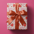 Red and pink christmas wrapping paper with pinwheel Santa hats and stars on cream.