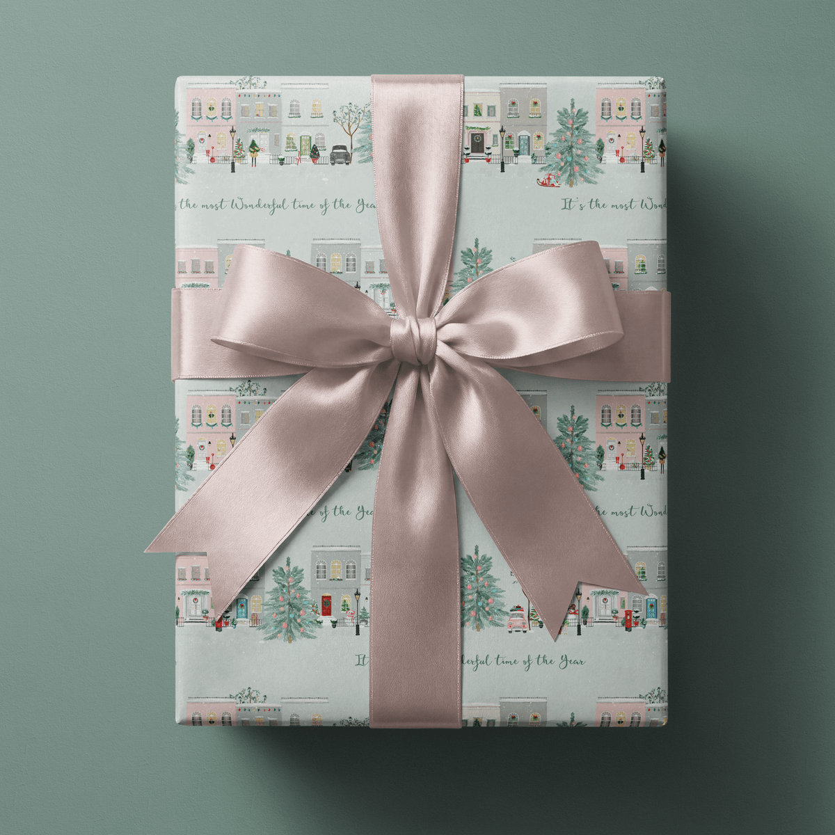 Gift wrapped in christmas village wrapping paper with pastel townhouses, tied with a blush pink ribbon bow