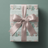 Gift wrapped in christmas village wrapping paper with pastel townhouses, tied with a blush pink ribbon bow