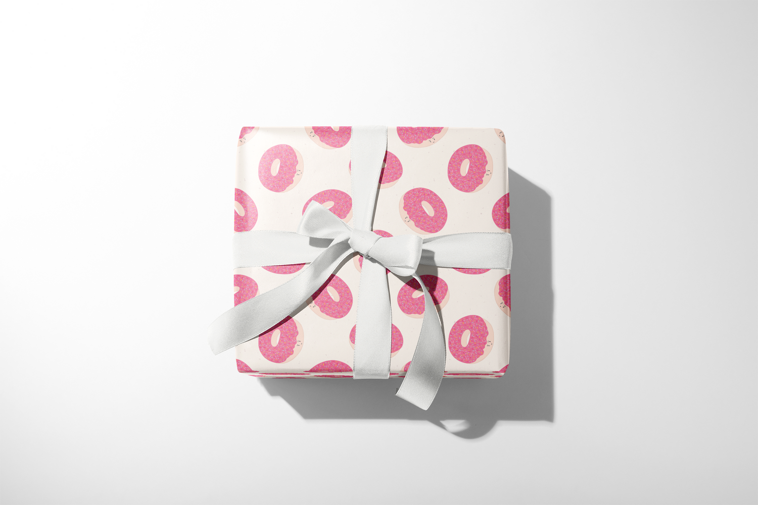 Alt Tag: Donut Wrapping Paper gift wrap with pink frosted donut pattern on neutral background, wrapped present with white ribbon