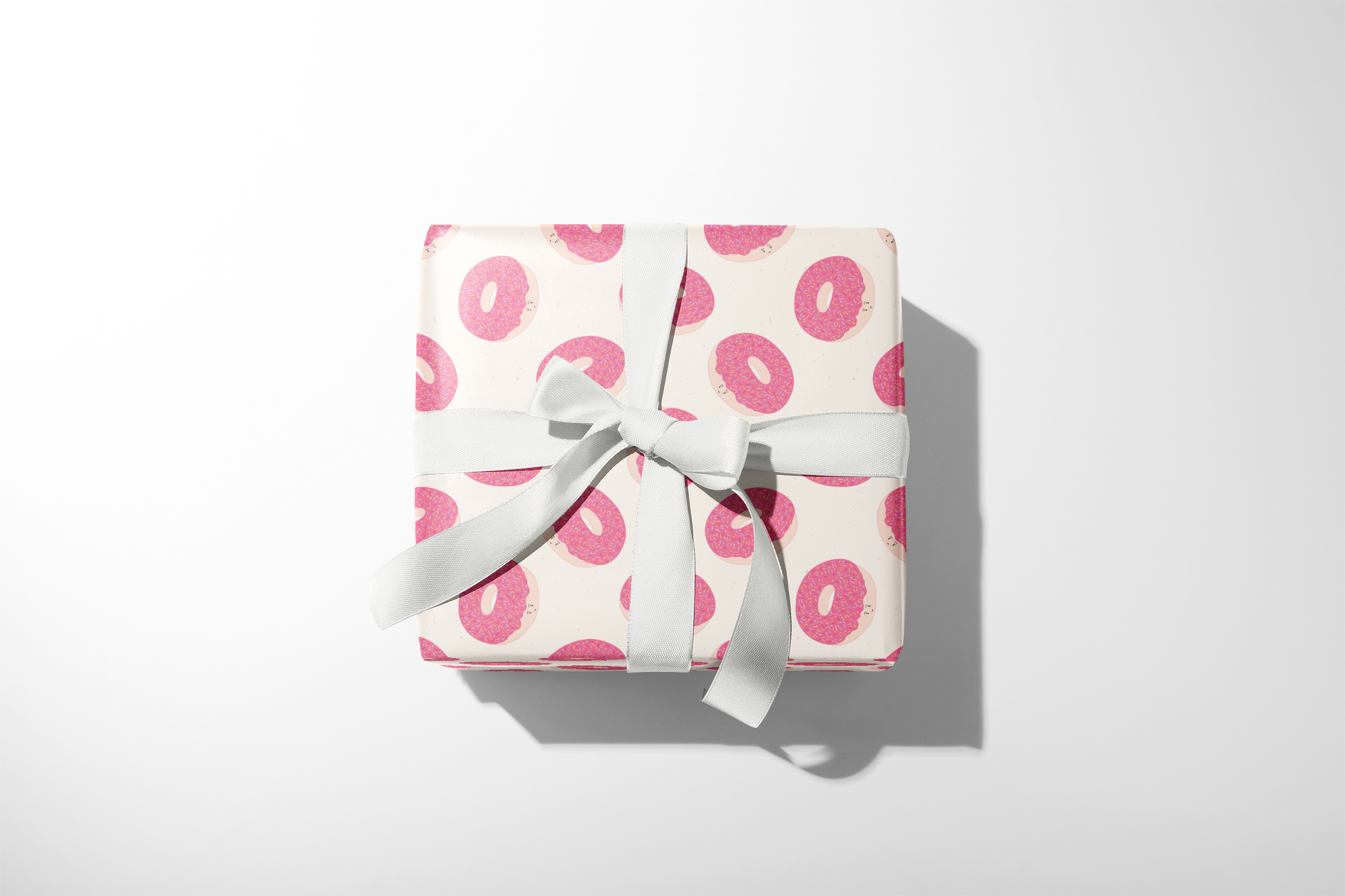 Alt Tag: Donut Wrapping Paper gift wrap with pink frosted donut pattern on neutral background, wrapped present with white ribbon